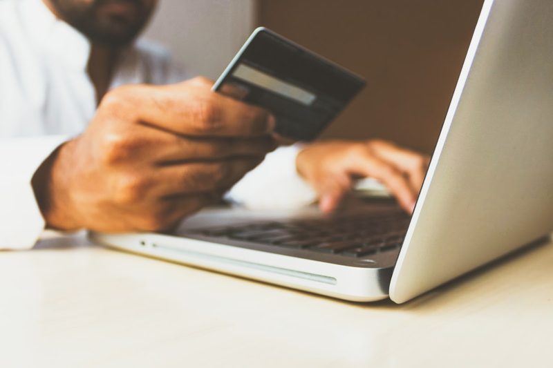 A person holding a bank card while typing on a laptop to complete an online purchase